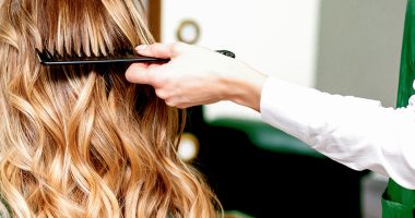 Back view of hairdresser combing wavy hair of a young blonde woman in a beauty salon